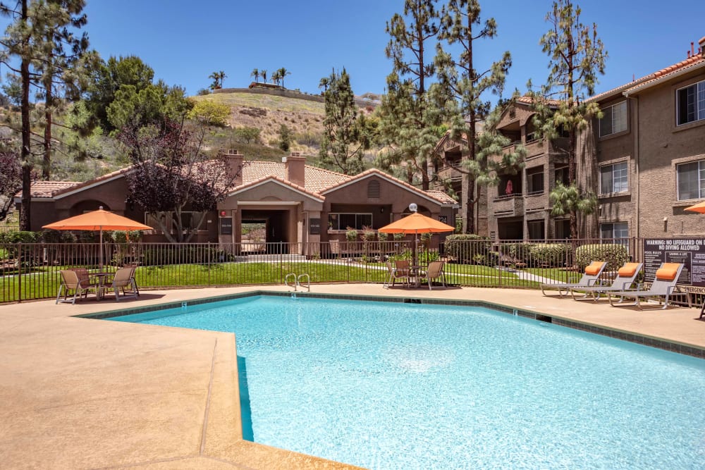 Beautiful resort-style swimming pool with lounge chairs and tables with umbrellas at Sierra Del Oro Apartments in Corona, California