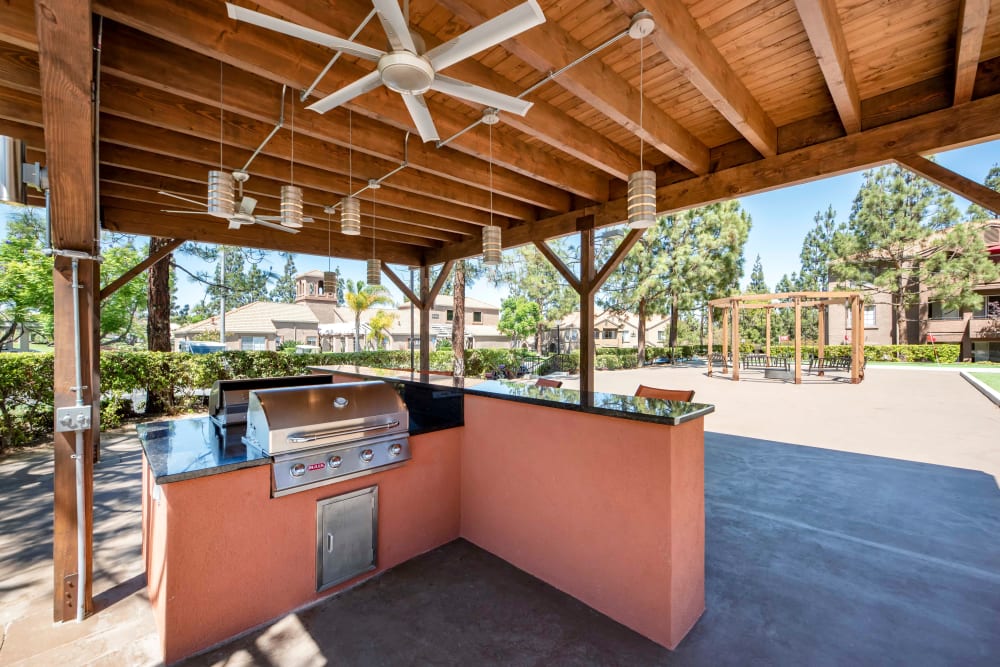Covered grilling area with bar top seating and a fan at Sierra Del Oro Apartments in Corona, California