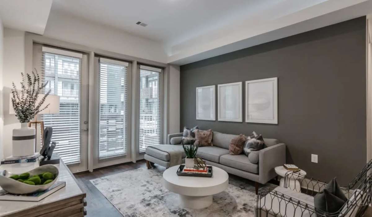 OneC1ty, Nashville, TN, Apartments - The Shay - Living Room With Accent Walls, Gray Sectional Sofa, Round Coffee Table, Accent Chair, Wall Art, Large Windows, and Glass Doors at The Shay in Nashville, Tennessee