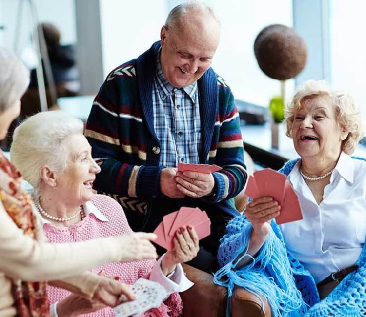 Resident friends playing cards and laughing together at Arcadia Senior Living Pace in Pace, Florida