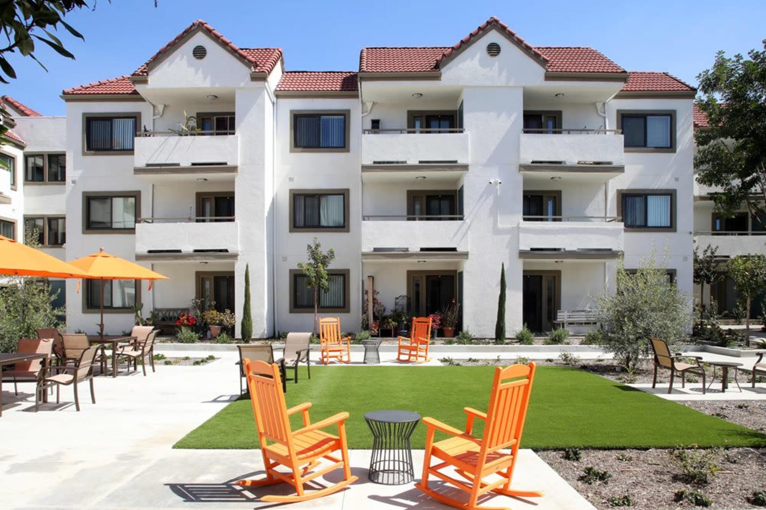 Outdoor area with tables, chairs and umbrellas at Sunny Garden Apartments in La Puente, California