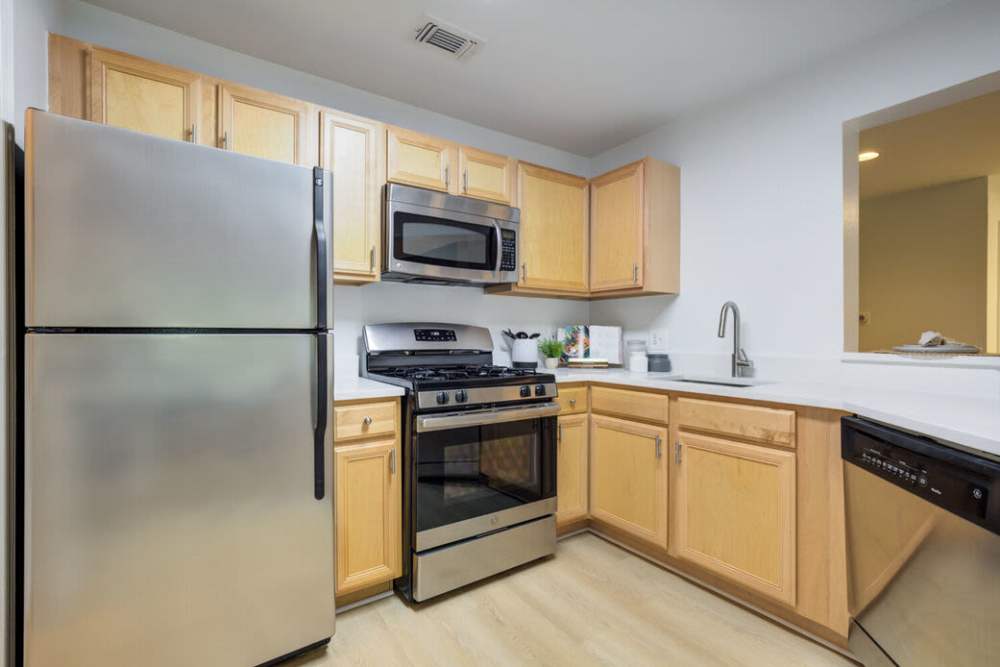 Modern kitchen with stainless steel appliances, granite countertops, wood-style flooring, and light wood cabinetry at J Harbor Park at North Point in Reston, Virginia