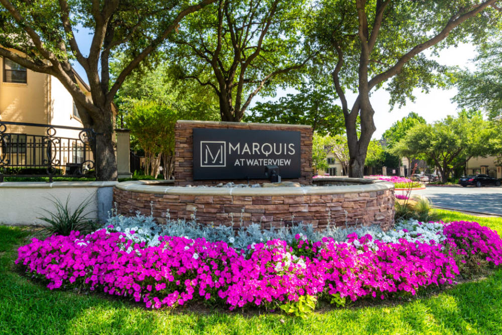 Property stone sign surrounded by colorful flowers and plants at Marquis at Waterview in Richardson, Texas