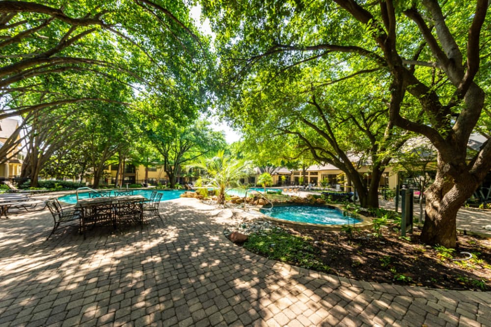 Pool deck area with tables and chairs covered by lush trees at Marquis at Waterview in Richardson, Texas