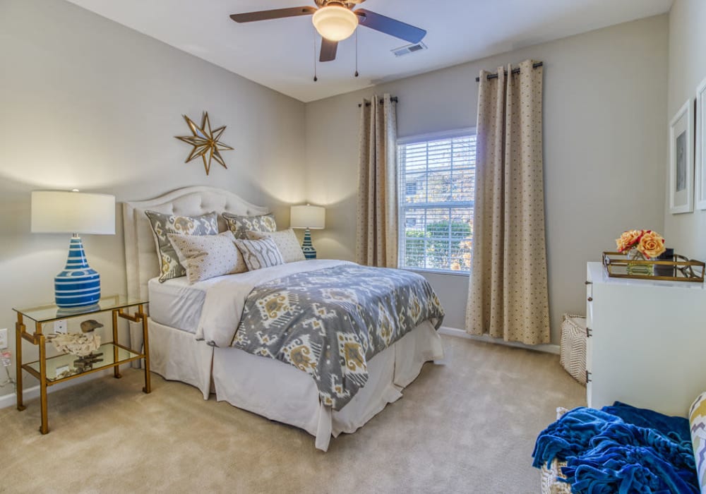 Beautifully designed bedroom with full bed, dresser, bed table, lamp, ceiling fan, and large window with drapes at at Everwood at The Avenue in Murfreesboro, Tennessee