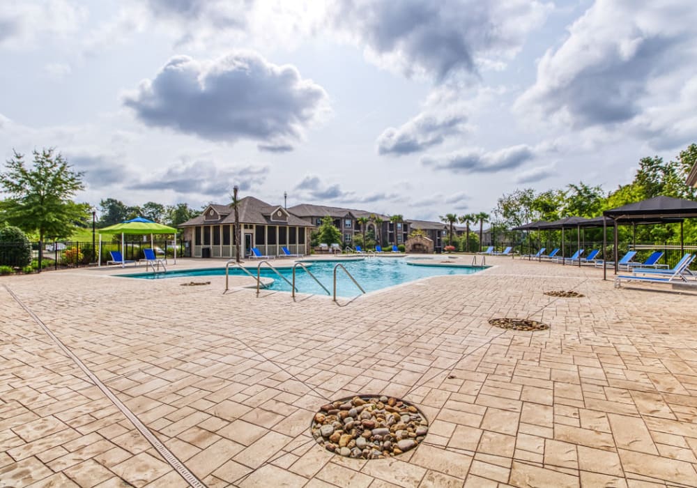 Resort-style swimming pool, vast tanning deck with many blue, chaise lounge chairs, and beautiful stone clubhouse surrounded by plants at Glass Creek in Mt Juliet, Tennessee