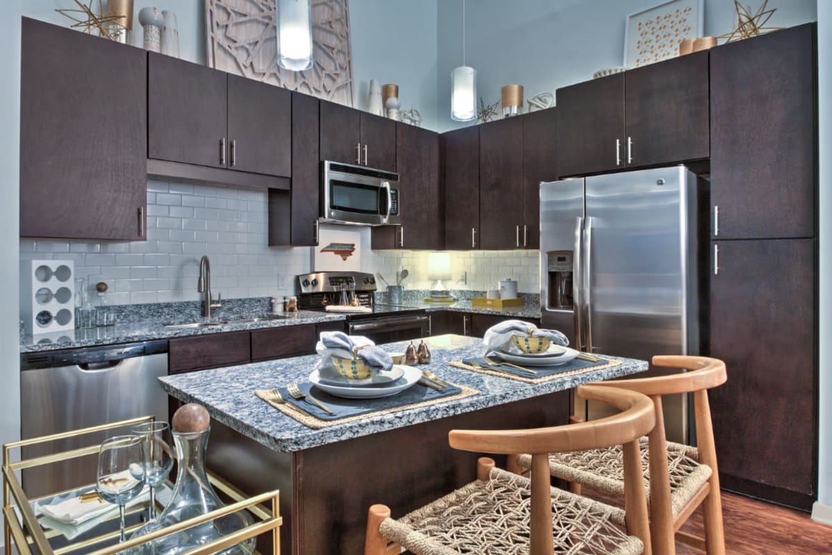 Chic styled kitchen with stainless steel appliances, granite counters, and dark wood cabinets at Marq Midtown 205 in Charlotte, North Carolina