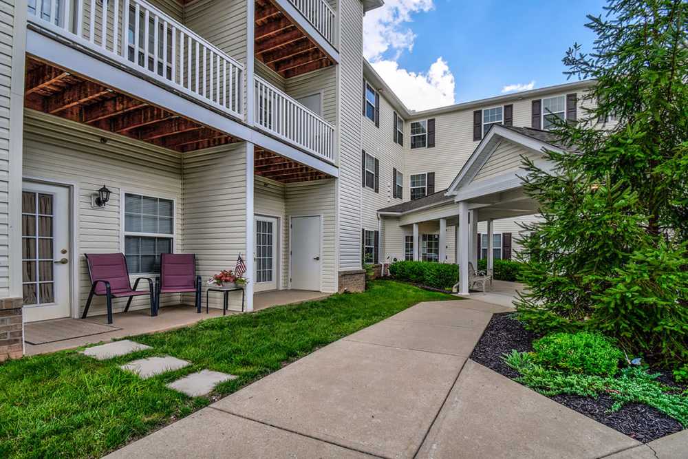 Ground-level patio with two chairs, landscaped grass, and a covered entrance to the apartment community at Norwood Greene Senior Living in Marietta, Ohio