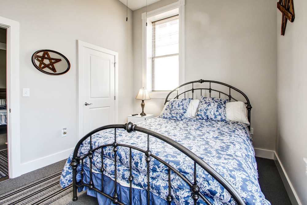 Cozy bedroom with a patterned blue bedspread, natural light from window, and decorative wall art at Lloyd House II in Menominee, Michigan