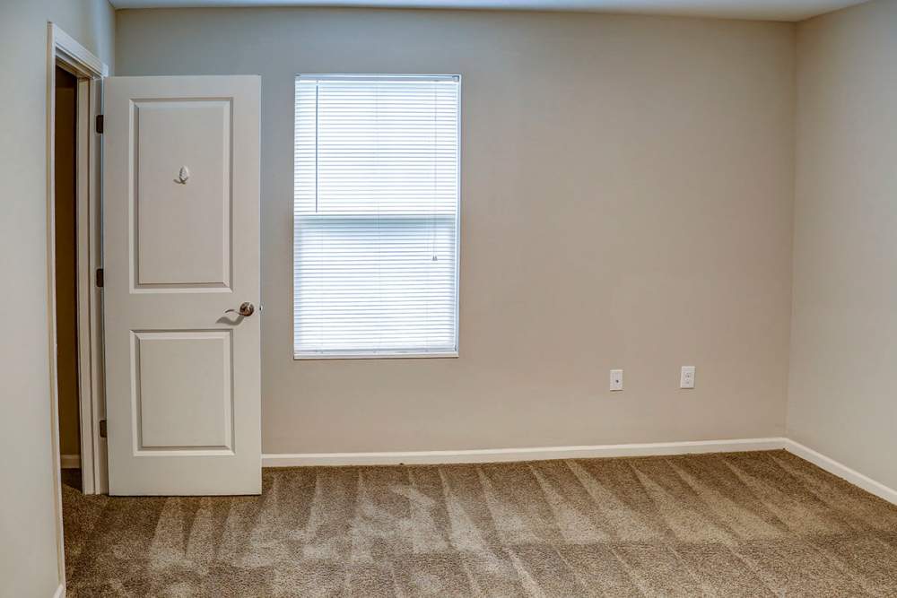 Empty room with beige walls, carpeted flooring, and a window with blinds at Brea's Crossing Senior Living I in Shelbyville, Kentucky