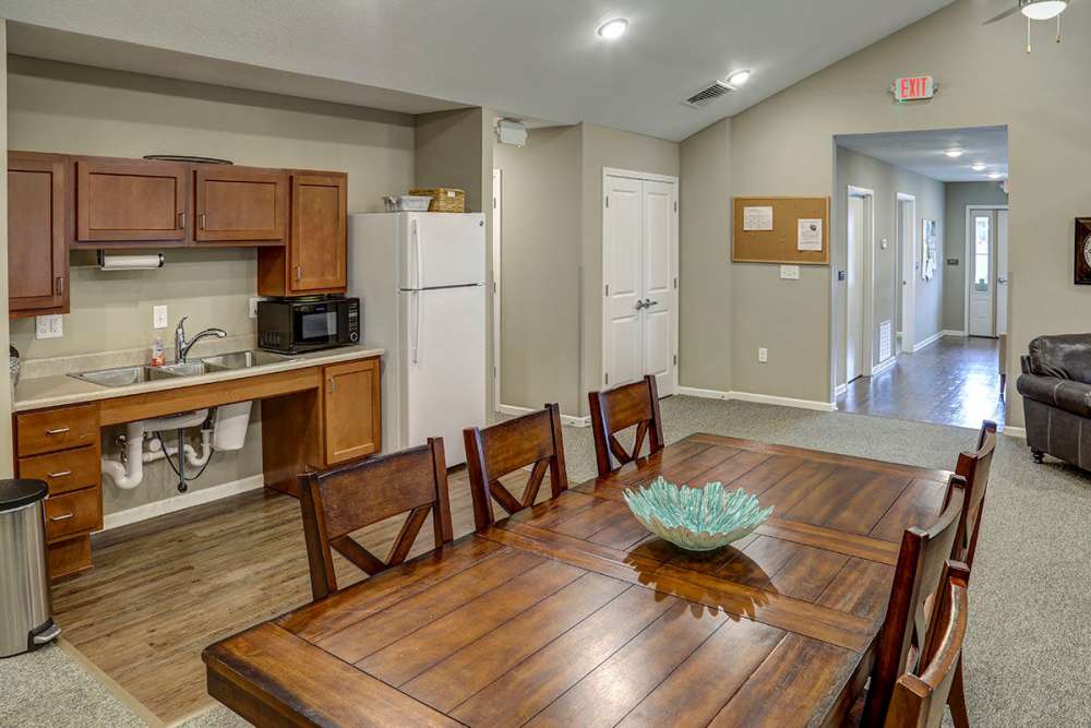 Open layout kitchen with granite countertops and stainless steel appliances, wood-style flooring, dining table in living area at Brea's Crossing Senior Living I in Shelbyville, Kentucky