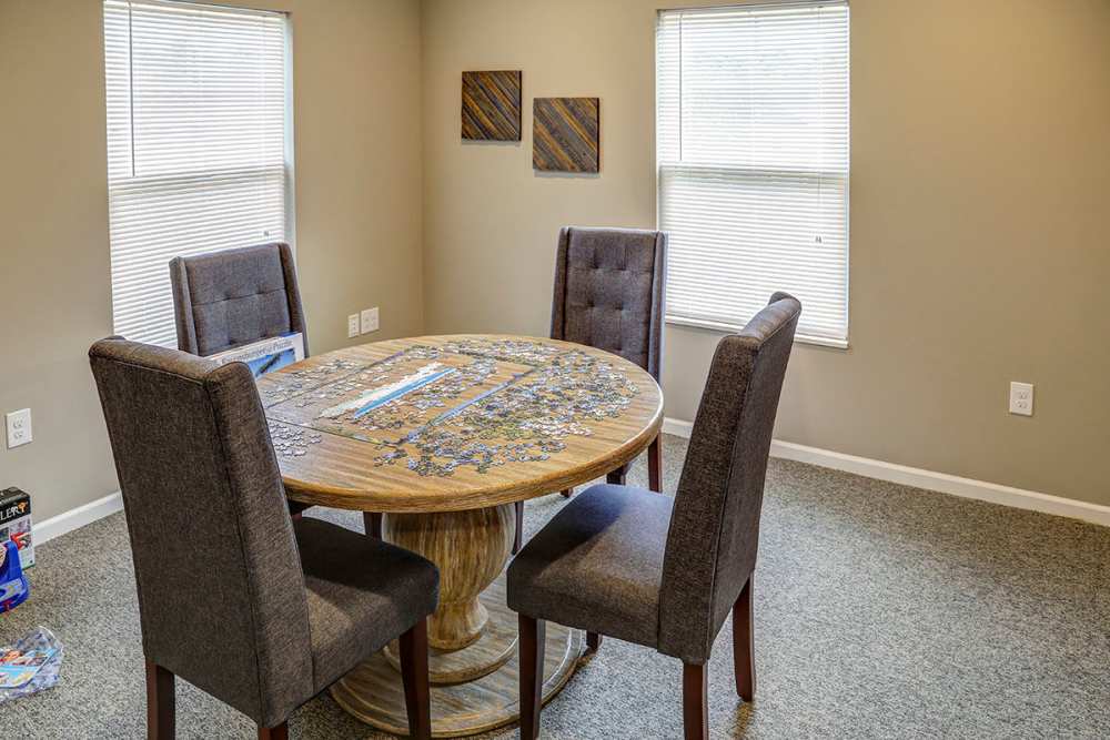 Dining area with four upholstered chairs around a round wooden table with puzzle pieces scattered on top at Brea's Crossing Senior Living I in Shelbyville, Kentucky
