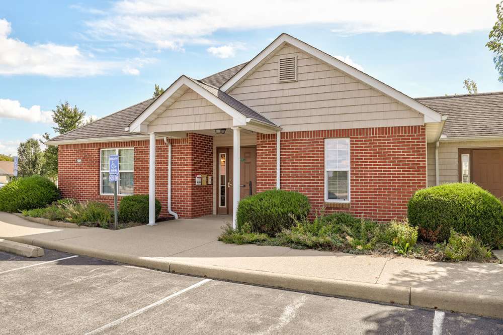 Brick apartment community entrance with manicured landscaping and accessible parking at Heritage Greene in Washington Court House, Ohio