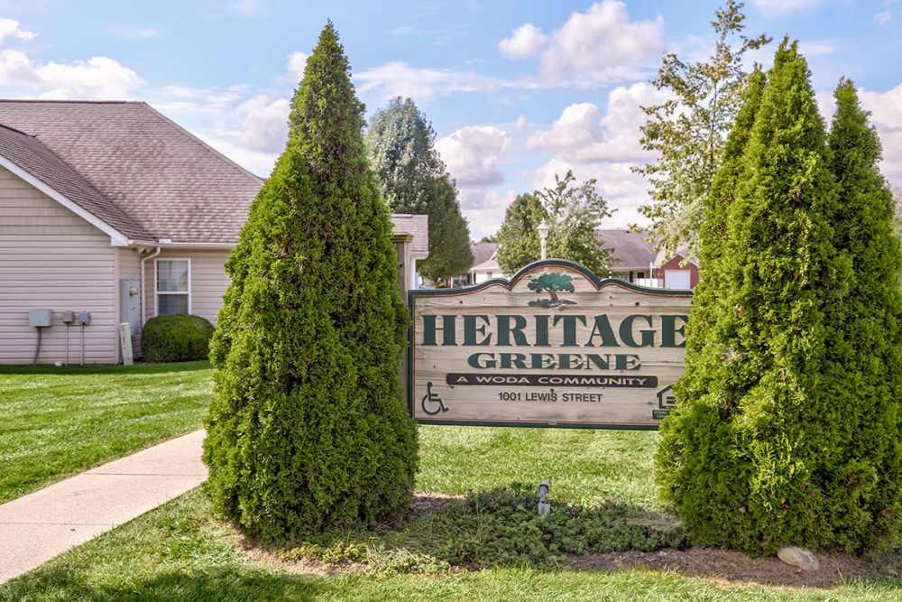 Community sign surrounded by manicured shrubs and green grass under a clear blue sky at Heritage Greene in Washington Court House, Ohio