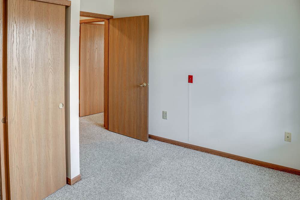 Empty room with beige carpet, two wooden doors, and neutral walls, featuring a simple layout at Heritage Greene in Washington Court House, Ohio