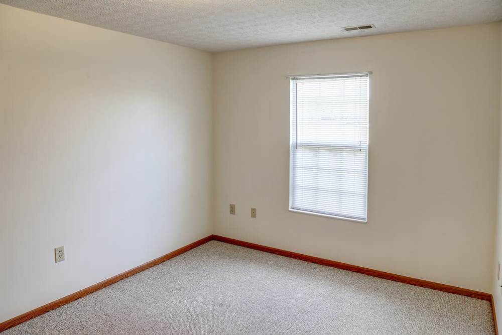 Empty room with carpet flooring and a window featuring blinds at Heritage Greene in Washington Court House, Ohio