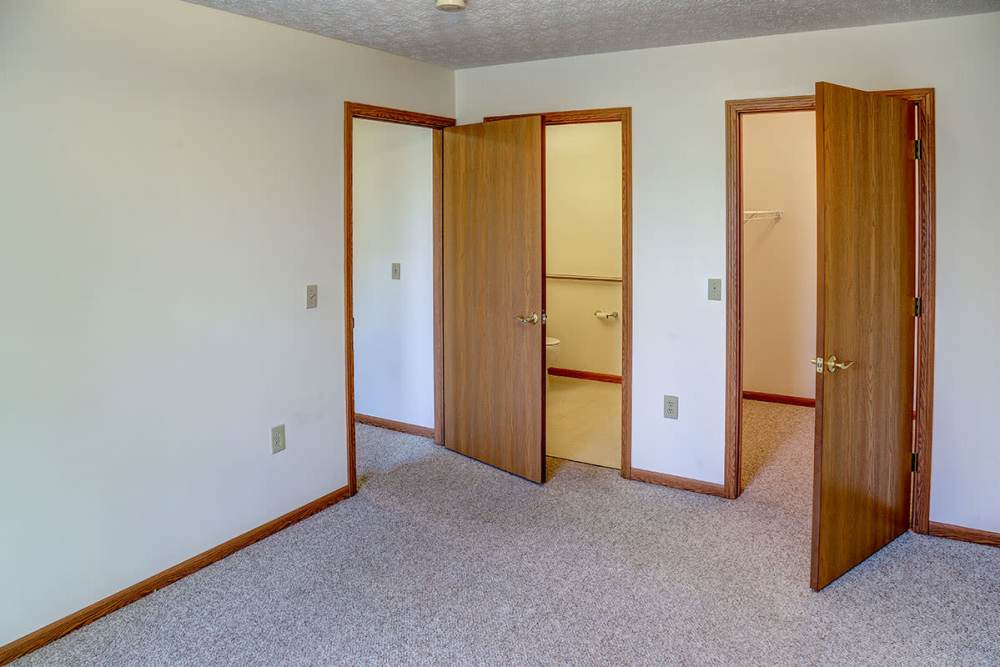 Spacious bedroom with carpeted flooring and multiple doorways leading to closets and bathroom at Heritage Greene in Washington Court House, Ohio