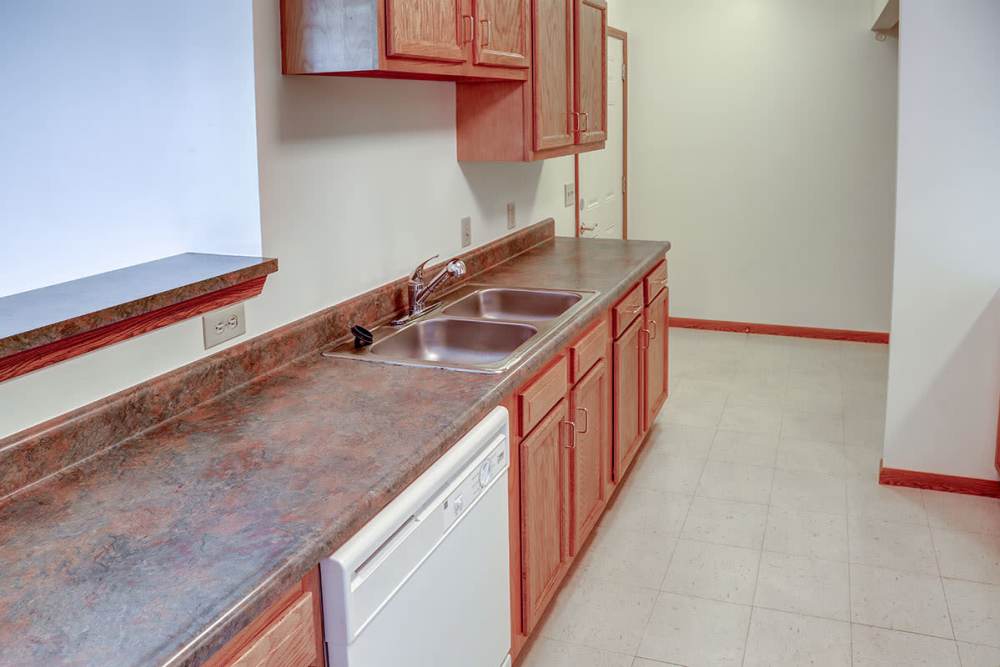 Modern kitchen with wood cabinetry, double sink, and dishwasher, featuring a spacious layout at Heritage Greene in Washington Court House, Ohio