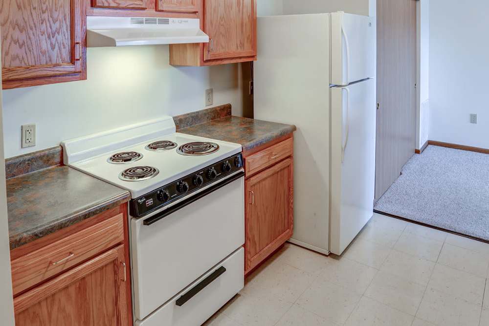 Kitchen with white appliances, electric stove, and wood cabinetry, featuring open layout and easy access to living area at Heritage Greene in Washington Court House, Ohio