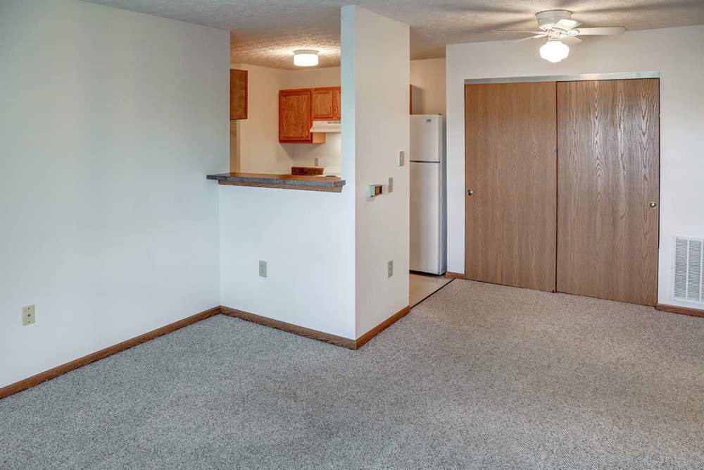 Spacious living area with carpeted flooring and open layout leading to kitchen with wooden cabinets at Heritage Greene in Washington Court House, Ohio