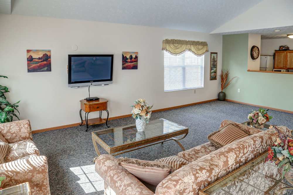 Cozy living room with floral sofas, coffee table, TV, and natural light from large window at Heritage Greene in Washington Court House, Ohio