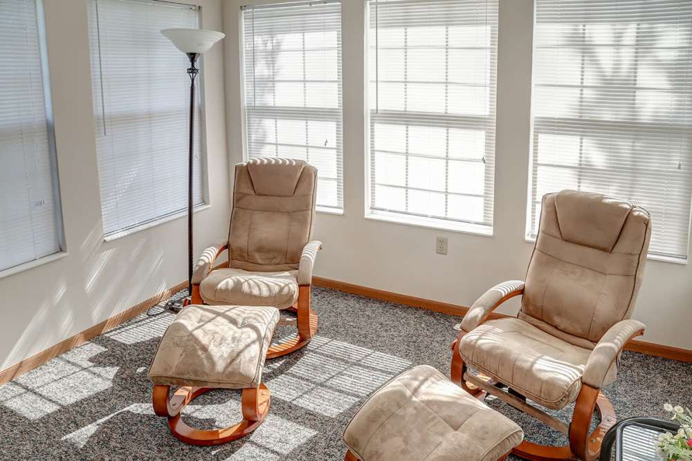 Bright sunroom with two plush rocking chairs and a floor lamp, carpeted flooring and large windows at Heritage Greene in Washington Court House, Ohio