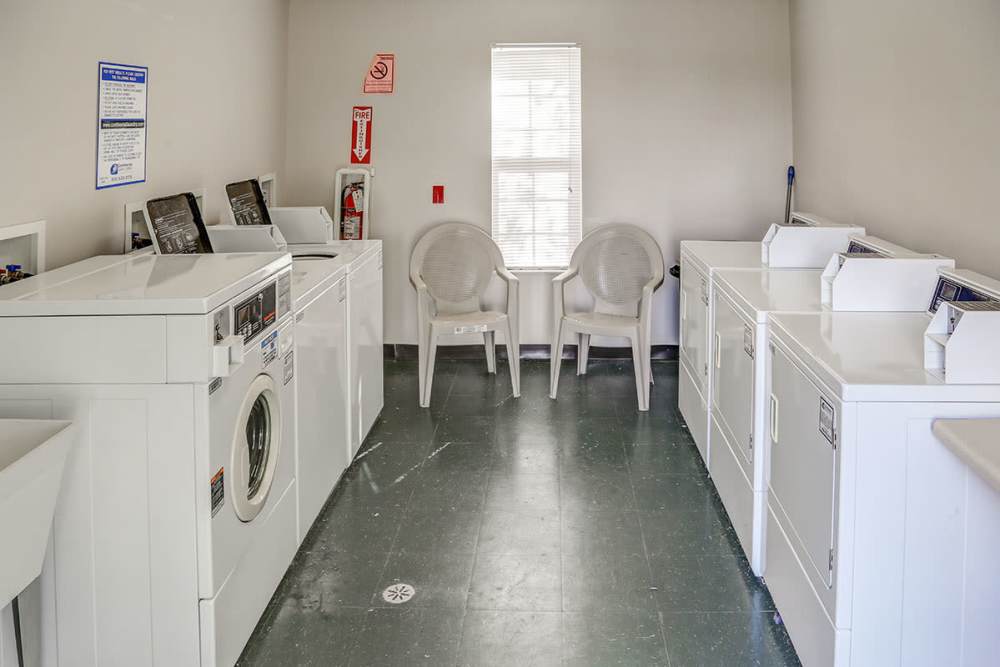 Bright laundry room with multiple white machines and two plastic chairs by a window at Heritage Greene in Washington Court House, Ohio