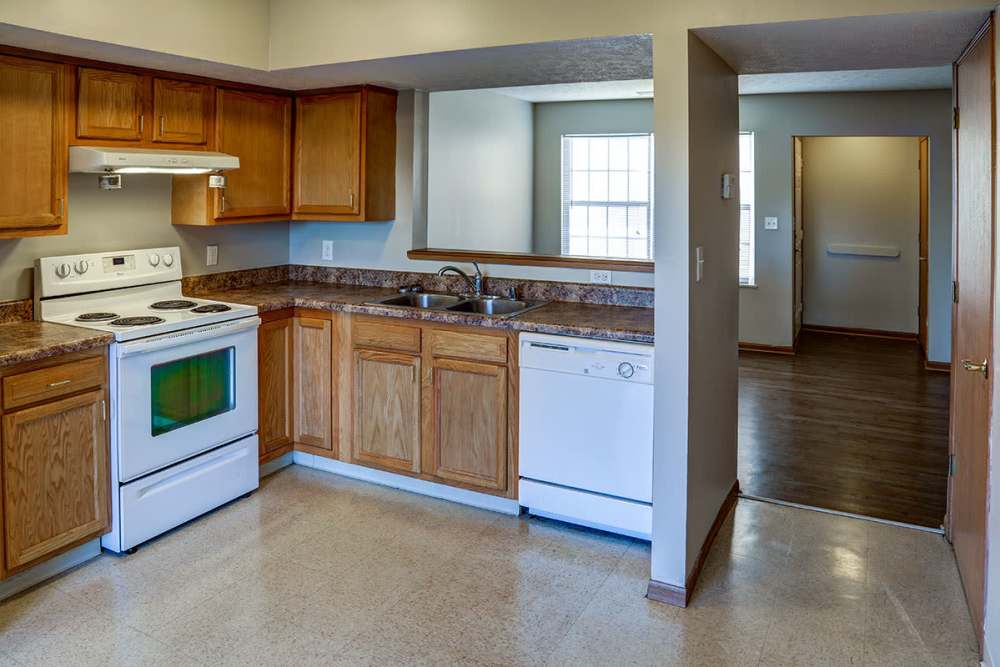 Bright kitchen with wood-style cabinets, white appliances, and open layout leading to living area at Mason Greene in Monticello, Kentucky