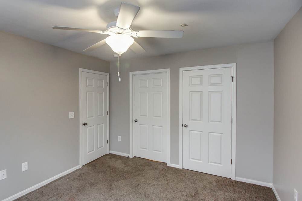 Empty bedroom with carpet flooring, ceiling fan, and three closed white doors at Northside Drive Apartments in Crossville, Tennessee