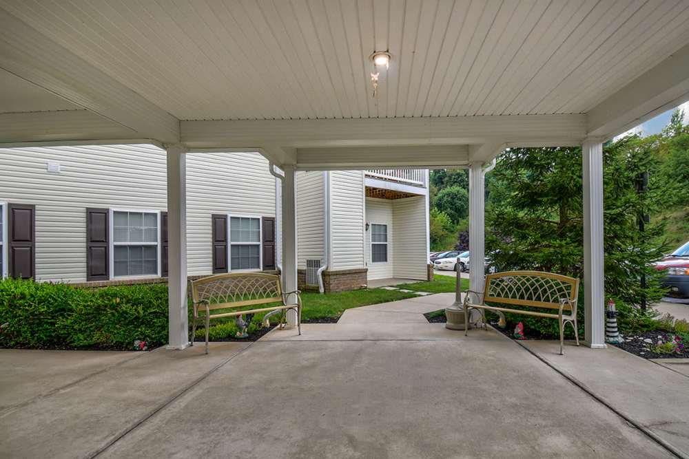 Covered entryway with seating and landscaped greenery leading to apartment community at Norwood Greene Senior Living in Marietta, Ohio