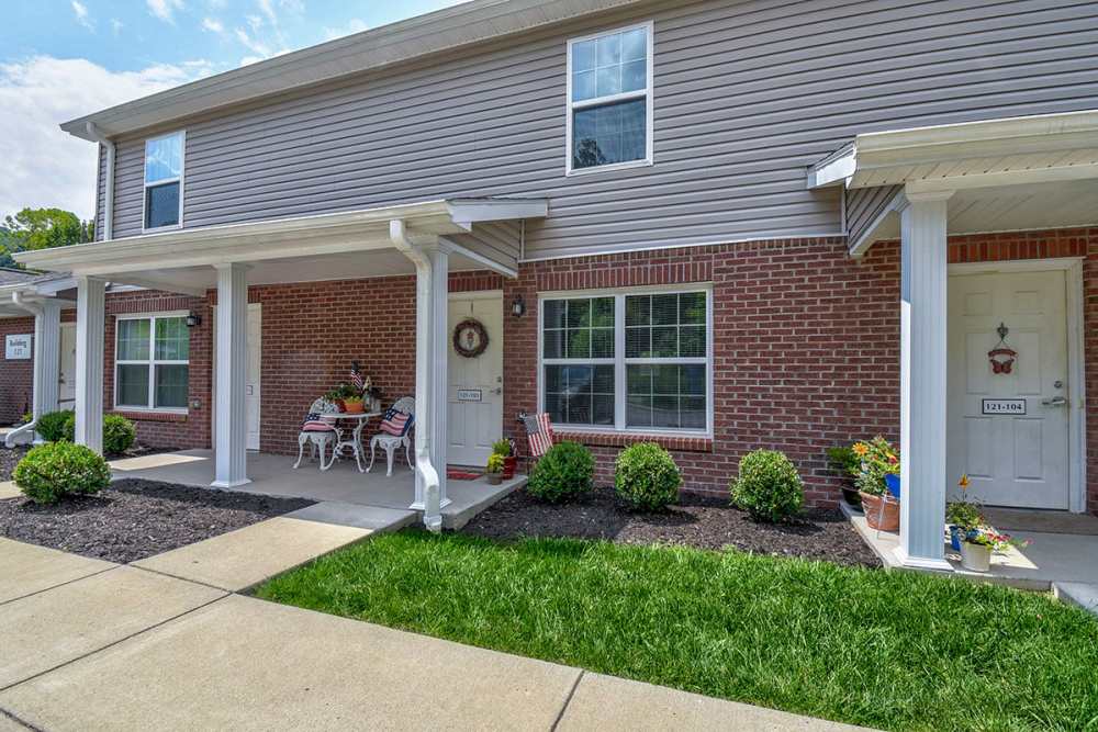 Charming apartment community with covered porches, landscaped gardens, and welcoming seating areas at Oak Valley Gardens in Glenville, West Virginia