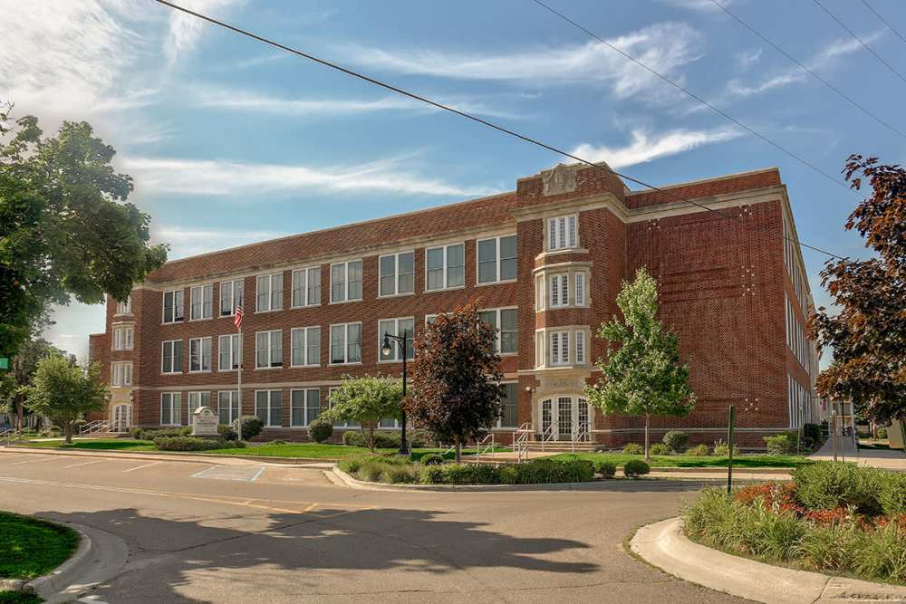 Historic brick building with large windows and landscaped green areas at Sycamore House Senior Living in Durand, Michigan