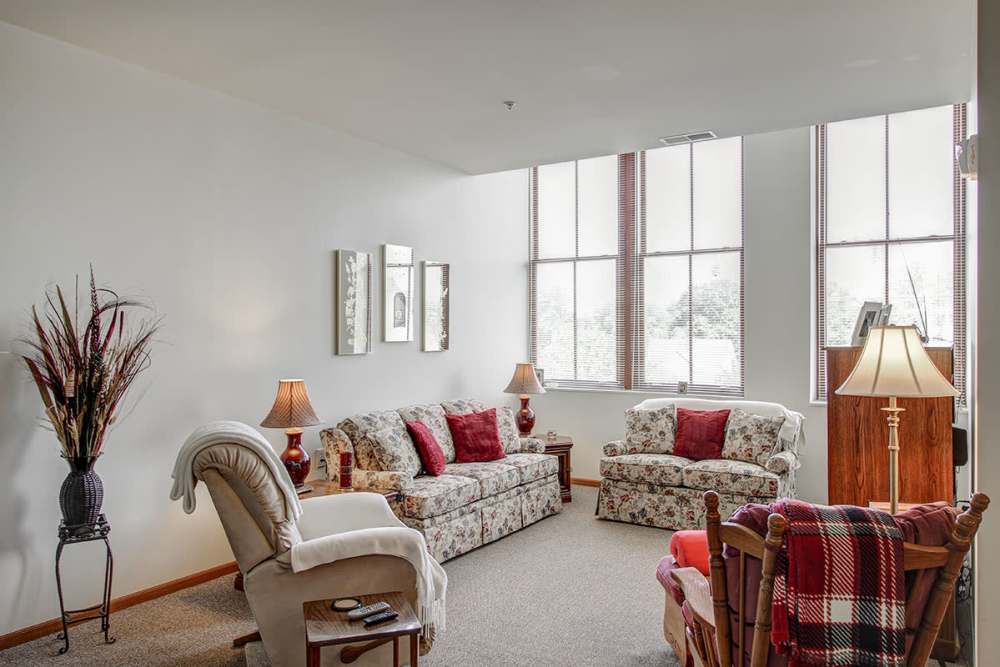 Cozy living room with floral furniture, large windows, and warm lighting accents at Sycamore House Senior Living in Durand, Michigan