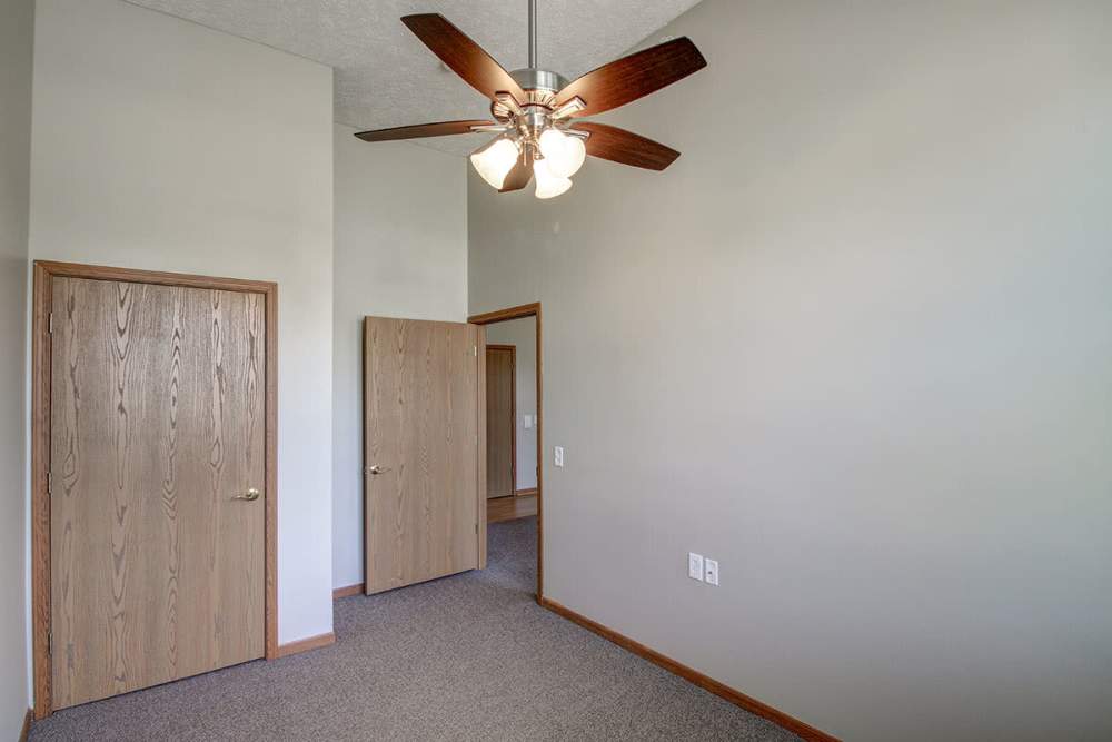 Spacious room with carpet flooring, ceiling fan, and two wooden doors leading to other areas at Sycamore House Senior Living in Durand, Michigan