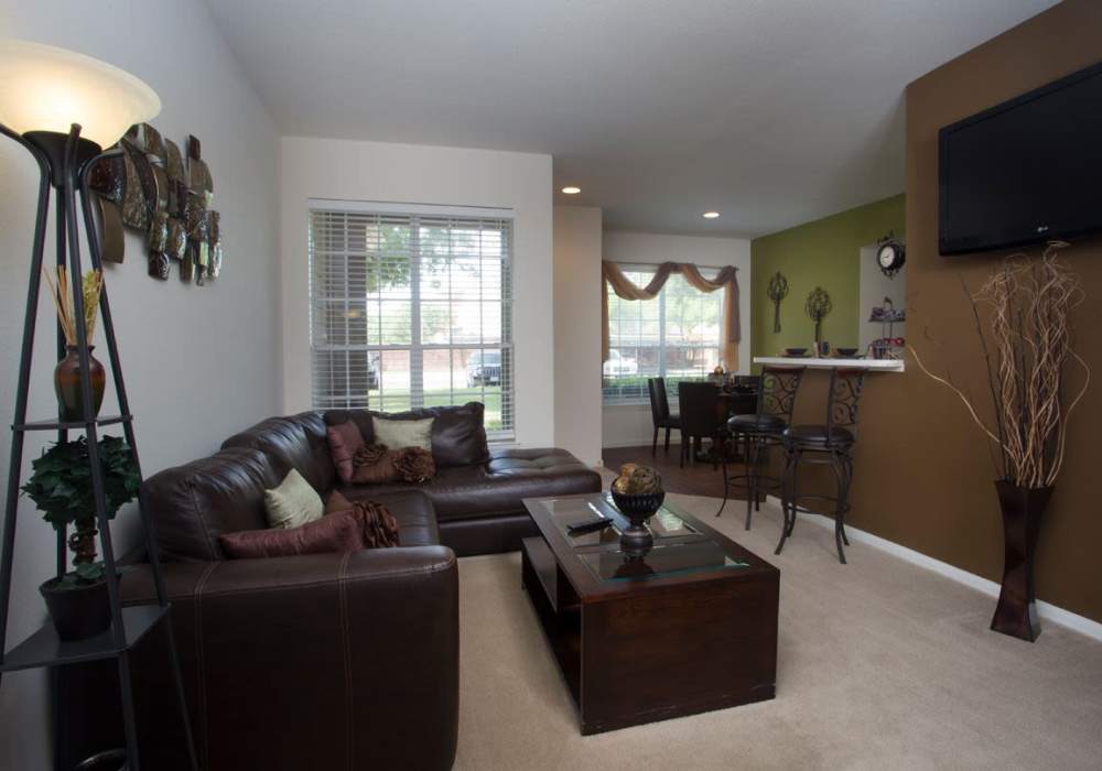 Cozy living room with brown leather sofa, decorative plants, and dining area in open layout at Rincon Apartments in McAllen, Texas
