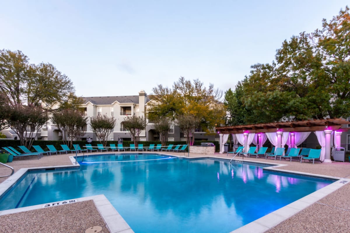 Pool with volleyball net, lounge chairs, and colorful lights under gazebo at sunset at Marquis at Stonegate in Fort Worth, Texas