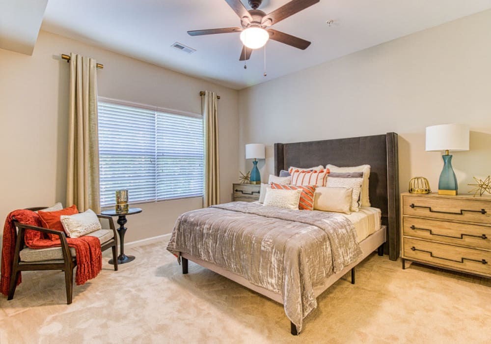 Spacious bedroom with carpet, ceiling lamp and fan, large window with queen bed, chair, dresser, and lamp at Greymont Village in Asheville, North Carolina