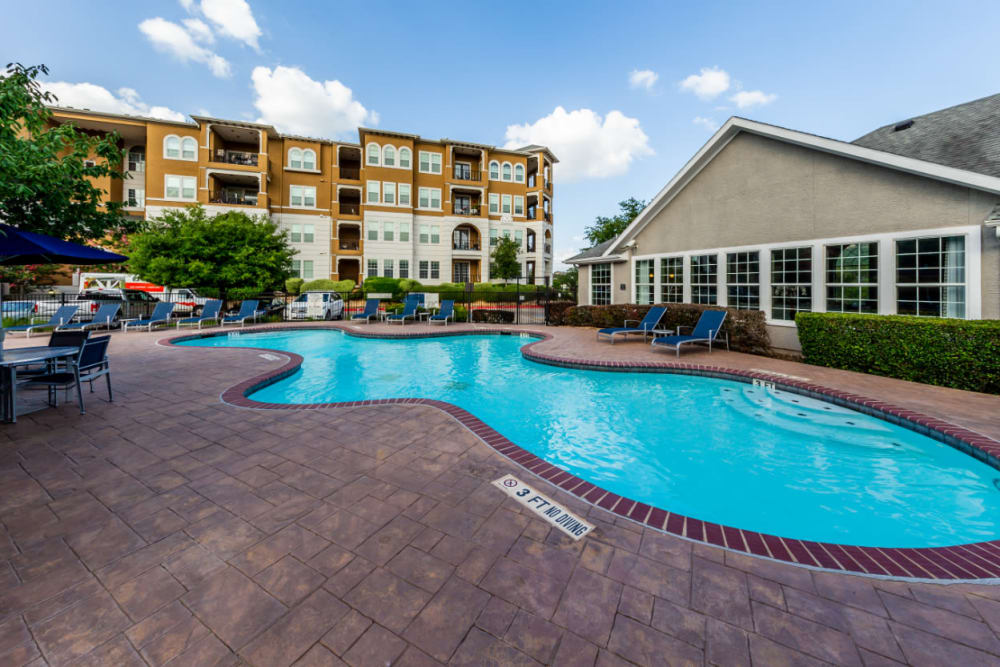 Shallow end of pool surrounded by lounge chairs and dining tables overlooking clubhouse at Marquis at Stone Oak in San Antonio, Texas