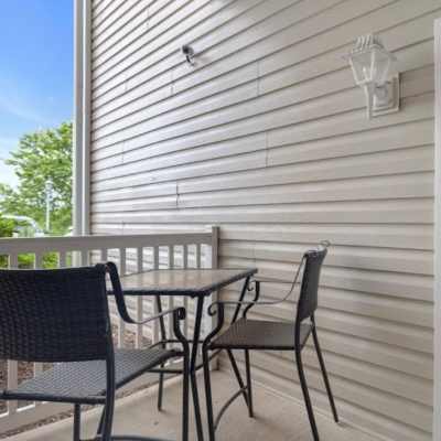 Small balcony with two chairs and a table, surrounded by light-colored siding and greenery at Castle Ridge Apartments in Pittsburgh, Pennsylvania