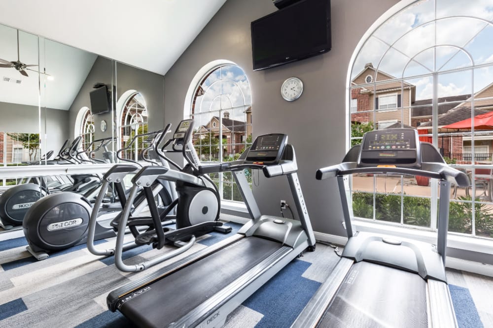 Treadmills and elliptical machine facing large monitor on wall and pool deck at Marquis on Park Row in Houston, Texas