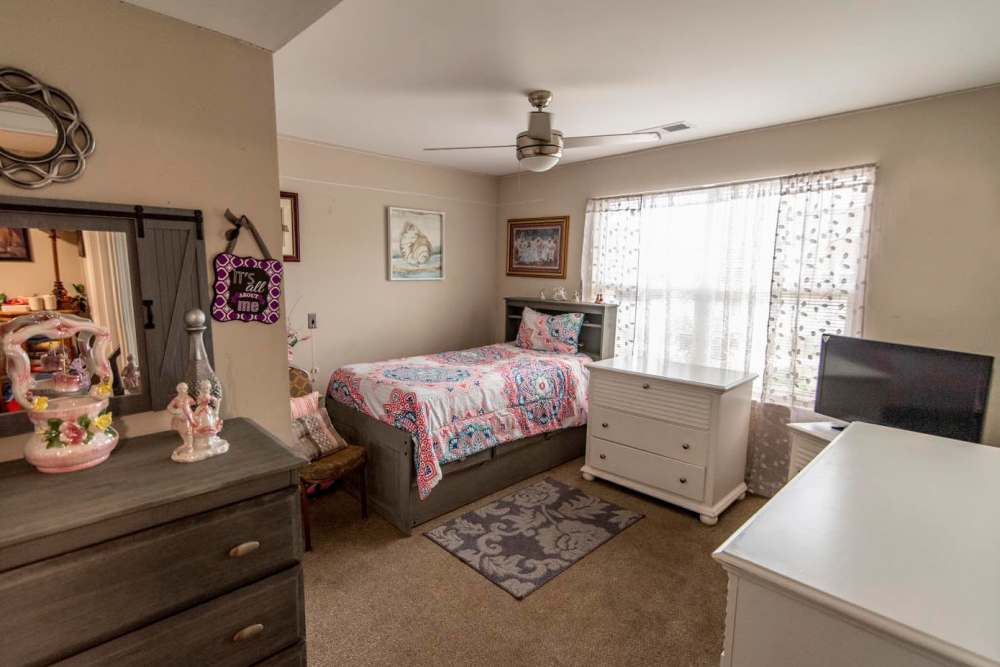 Cozy bedroom with a patterned bedspread, dresser, and window with sheer curtains at Butler Crossing II in Kingstree, South Carolina