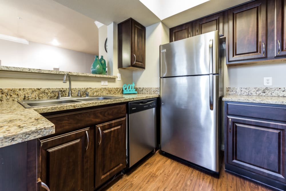 Modern kitchen with stainless steel appliances, granite counter tops, and wood flooring at Marquis at Stonegate in Fort Worth, Texas