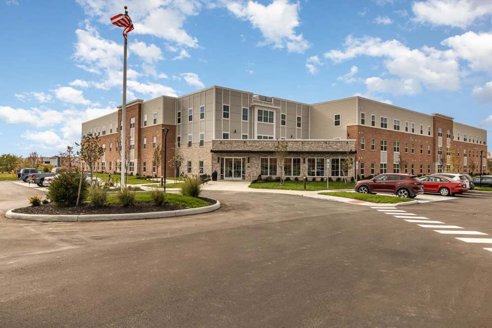 Modern apartment community with landscaped entrance and parking area under a clear blue sky at Haven Crossing in Walton, Kentucky