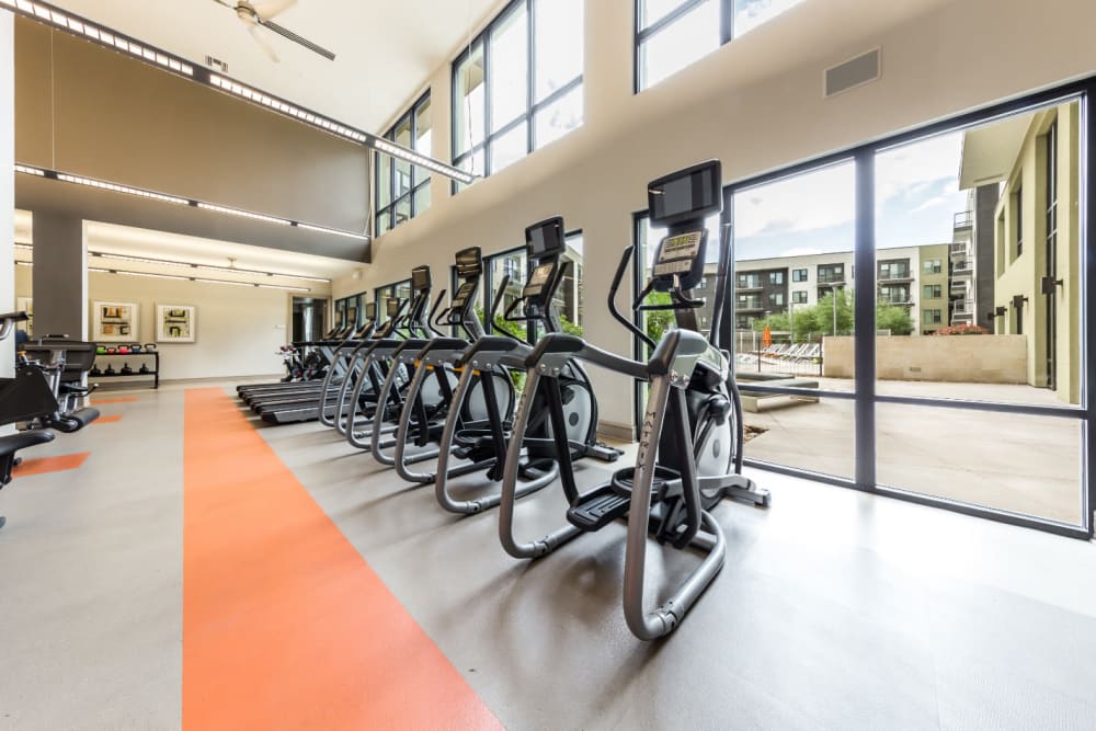 Multiple elliptical and treadmills lined up facing windows with view of pool deck at Marq Uptown in Austin, Texas