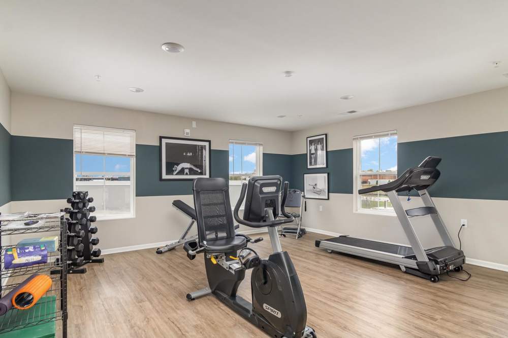 Bright fitness center with wood-style flooring, windows for natural light, and exercise equipment including treadmill and stationary bike at Haven Crossing in Walton, Kentucky
