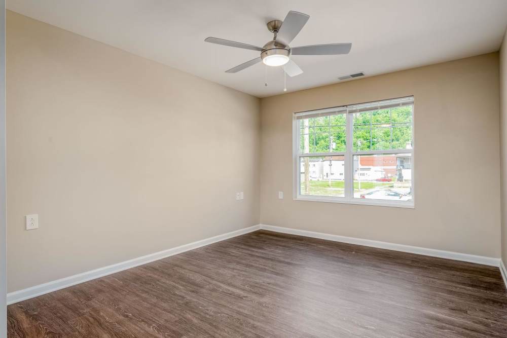 Spacious room with wood-style flooring, ceiling fan, and large window for natural light at Owens Greene in Wheeling, West Virginia