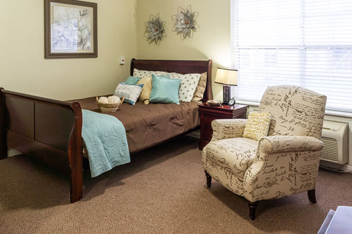 Model unit with bed and comfy chair at Plum Creek Place in Amarillo, Texas