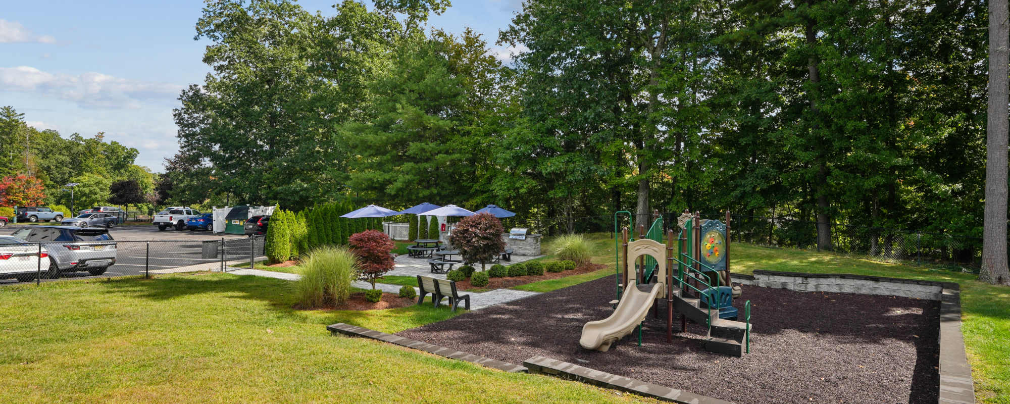 Community playground with slides, shade trees, and open green space at Highlands at Hudson in Hudson, Massachusetts