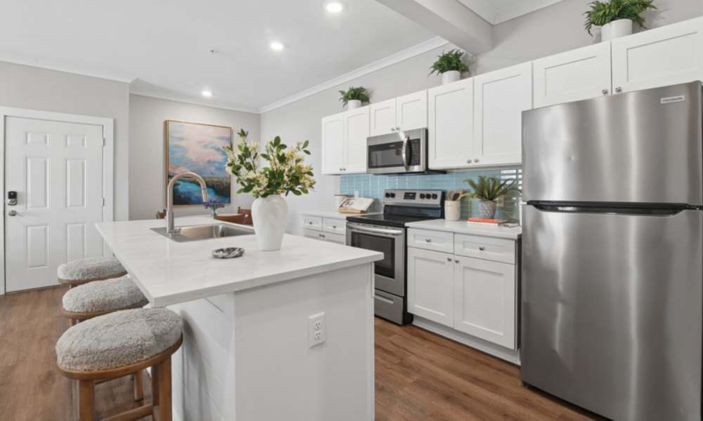 Modern kitchen with granite countertops, stainless steel appliances, and wood-style flooring, featuring a large island and pendant lights at Everett at Port Wentworth in Port Wentworth, Georgia