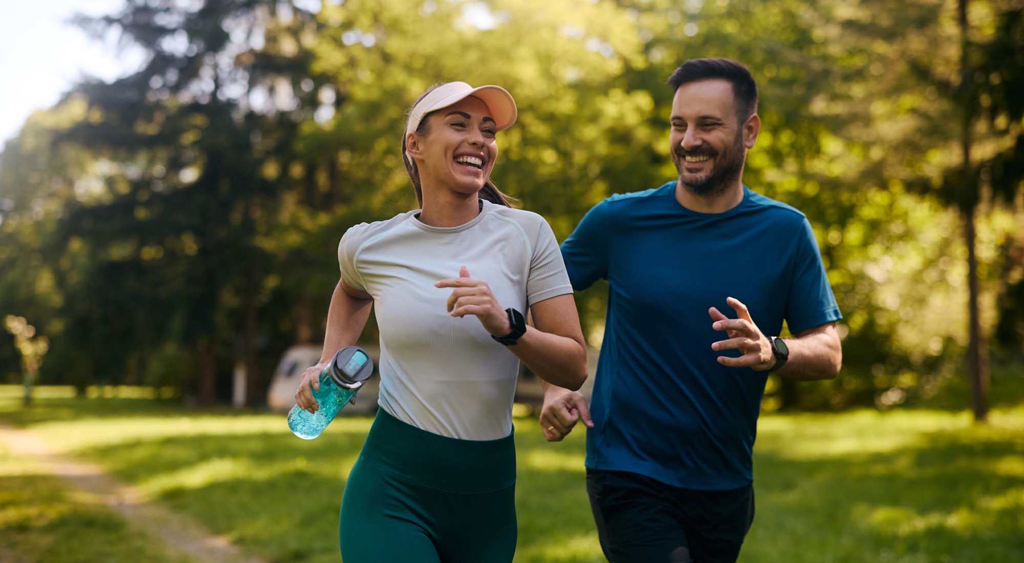 Couple jogging together on a sunny path surrounded by greenery, enjoying an active lifestyle at South Oak in Ames, Iowa